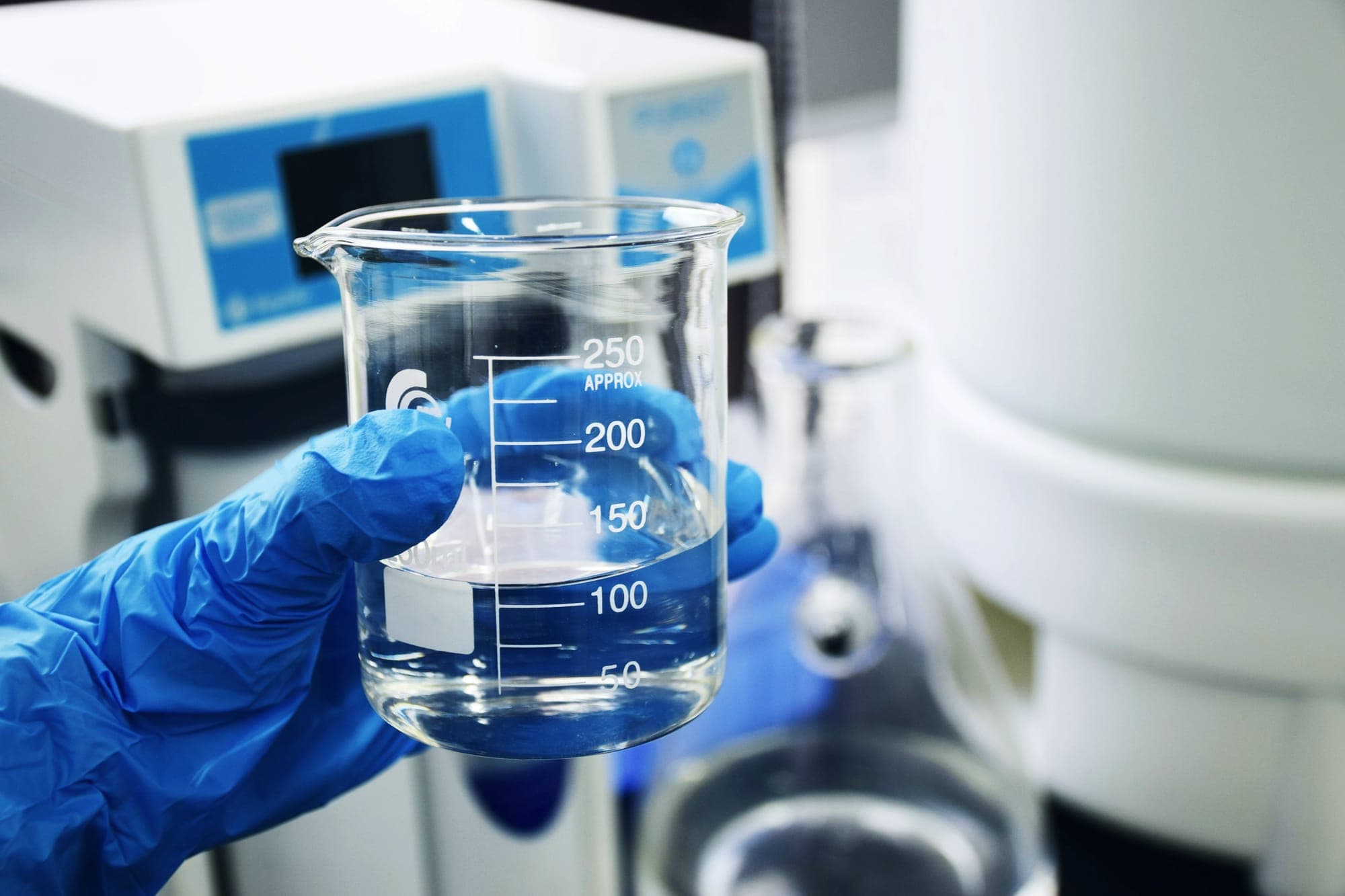 Gloved hand holding a beaker of purified water in a laboratory
