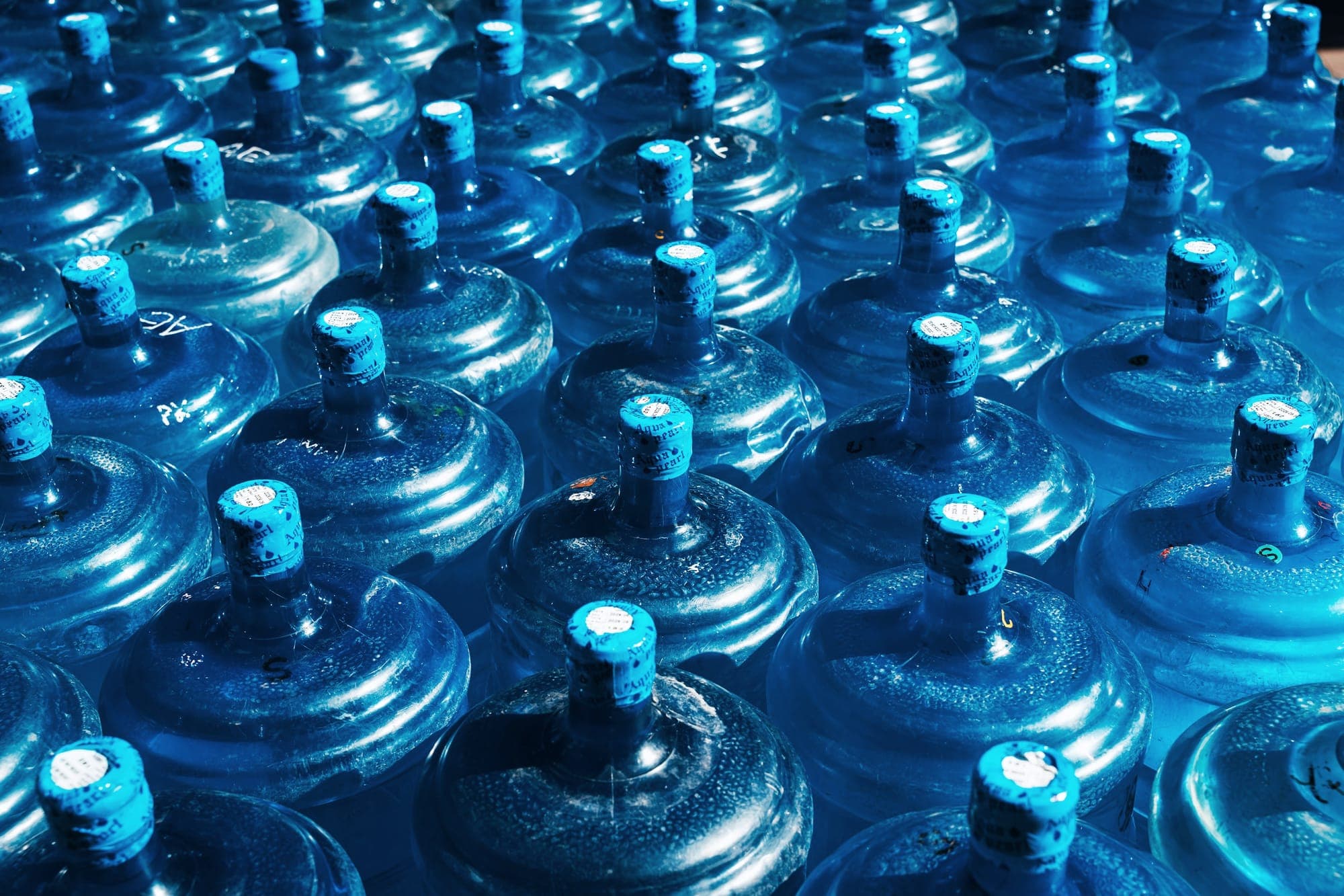 Rows of blue twenty-litre drinking water jars filled and capped at a bottling plant